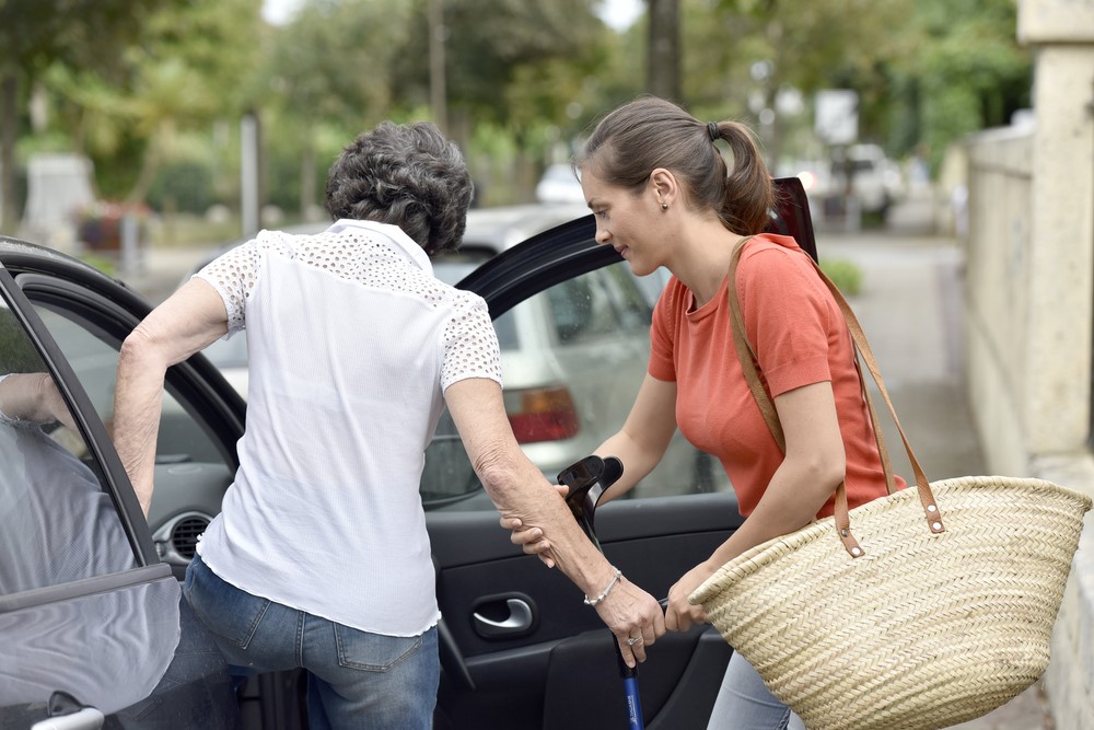 A carer helping a senior into a car