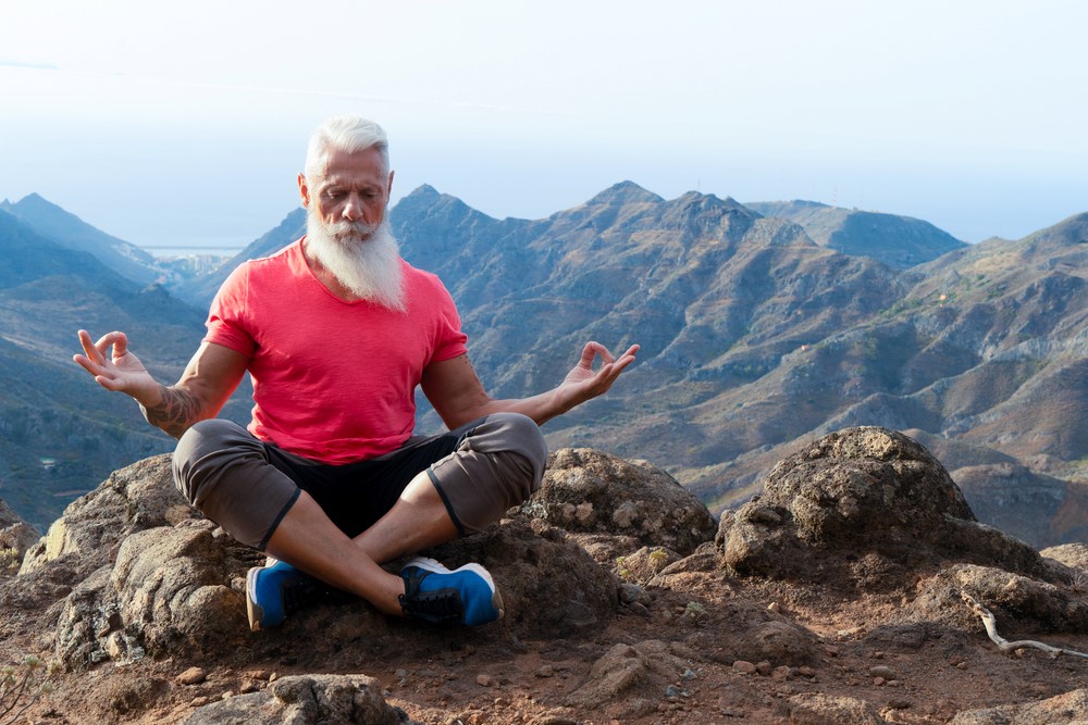 A senior man practicing yoga outside, as part of a mindfulness for seniors practice