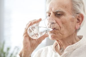 An elderly man drinking water and looking unhappy, highlighting the idea of persuading seniors to drink water