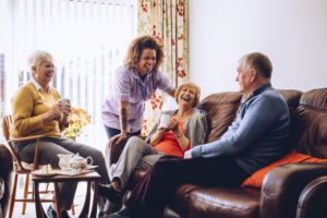 Three seniors laughing in a living room with one of their caregivers or family members