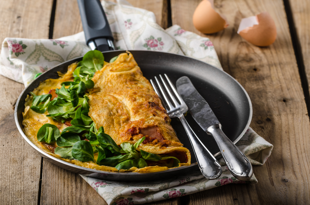 An omelet made using leafy greens on a plate with a knife and fork