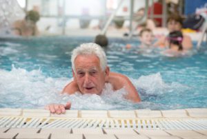 Senior in a pool, holding onto the side and kicking.