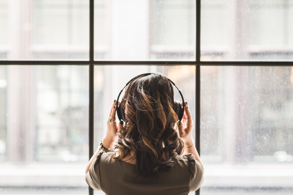 Young woman looking out of a window wearing headphones, highlighting the benefits of music therapy for seniors