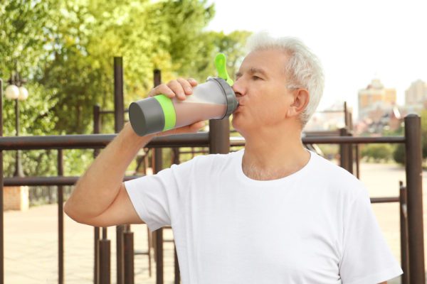 An active senior man drinking a protein shake that could be from Ensure or Boost