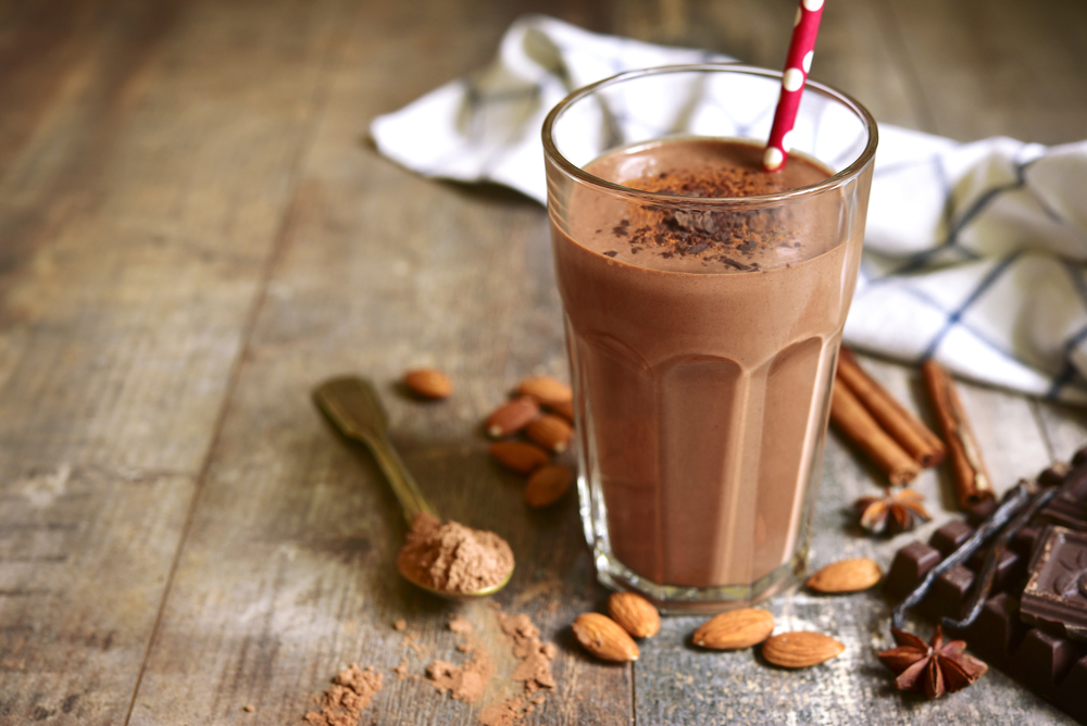 A chocolate protein shake on a wooden table with almonds