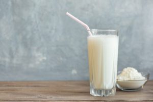 A glass of vanilla protein shake next to the powder, highlighting the question of how long the elderly can live on Ensure