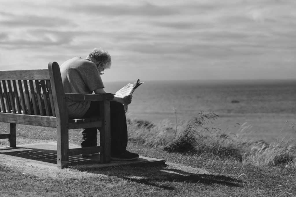 A senior man sitting and reading the paper by the beach, highlighting the idea of isolation in seniors