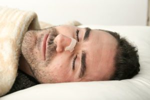 A man using a Breathe Right Nasal Strip to prevent him from snoring