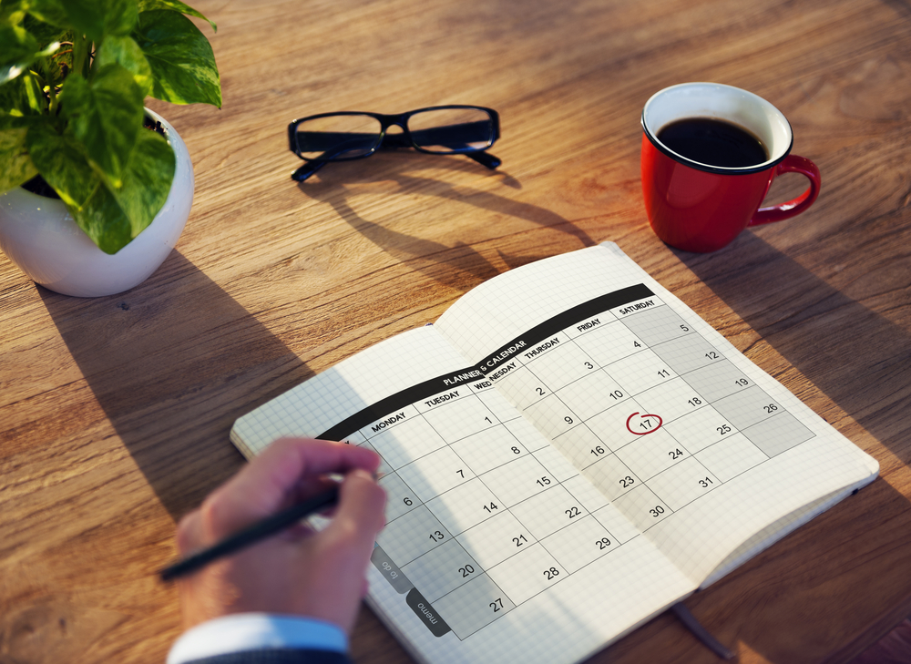 Organizing with a calendar in a journal on a desk that includes a plant, a cup of coffee, and a pair of glasses