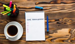 A to-do list on a wooden table, along with a cup of coffee and a basket of pens