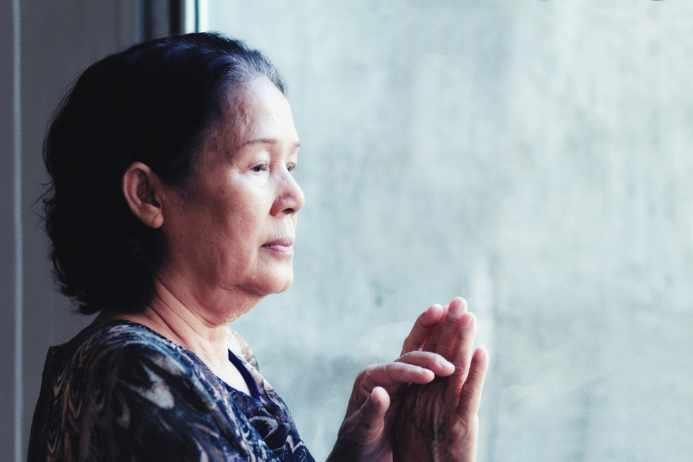 A lonely older adult Asian woman standing by the window