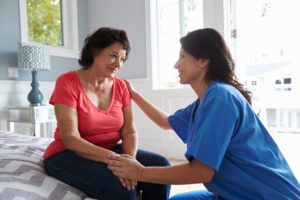 A woman or nurse talking with a senior who is sitting on the bed