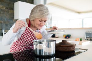 A senior woman cooking at home, highlighting the pros and cons of aging at home