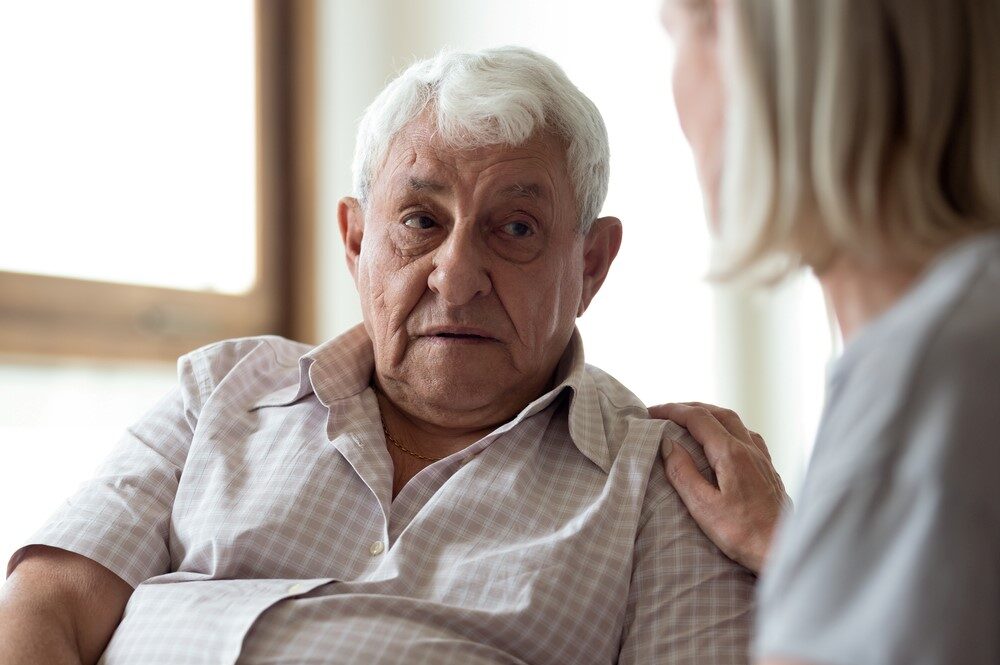 A middle aged woman comforting her aging father, focusing on the idea of talking to seniors