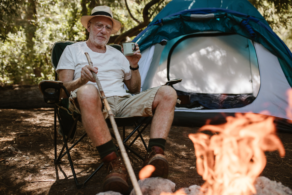 A senior camping and cooking with a pie iron