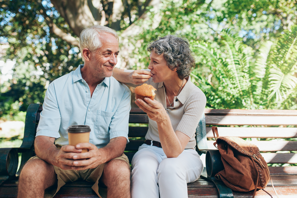 A senior couple sitting outside with coffee and snacks