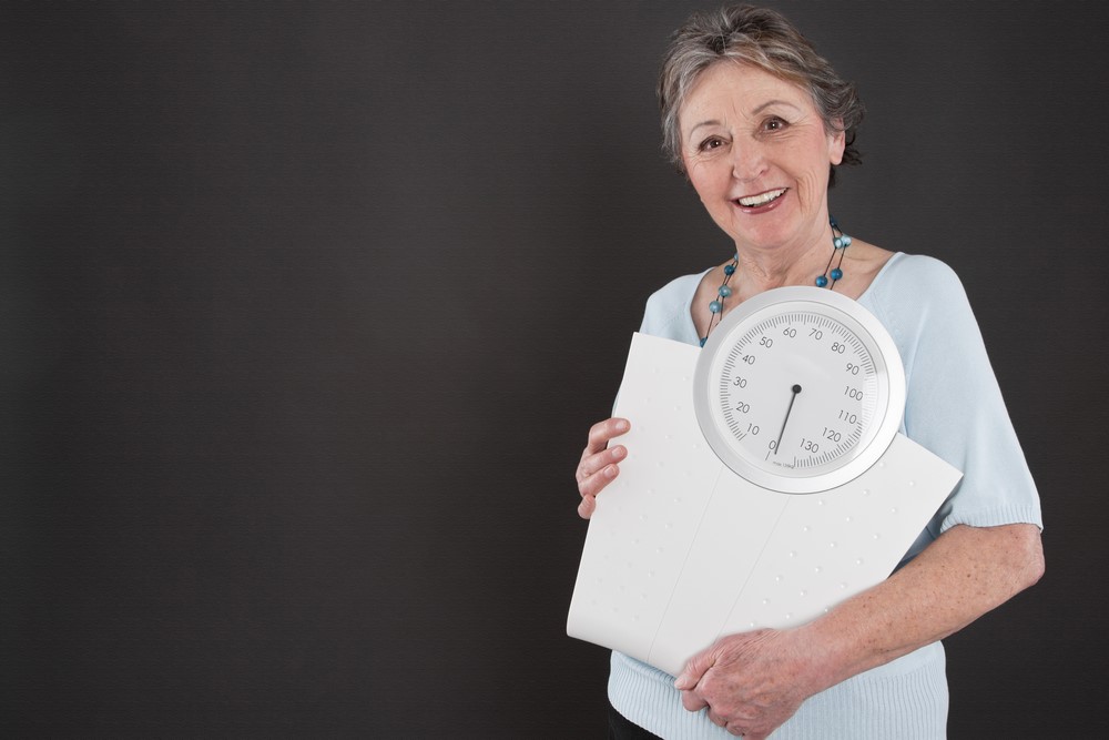 A senior woman with scales highlighting the idea of weight loss in seniors