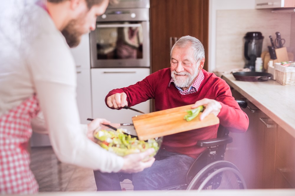 A senior man in a wheelchair, cooking with his adult son, showing that disability doesn't need to be limiting