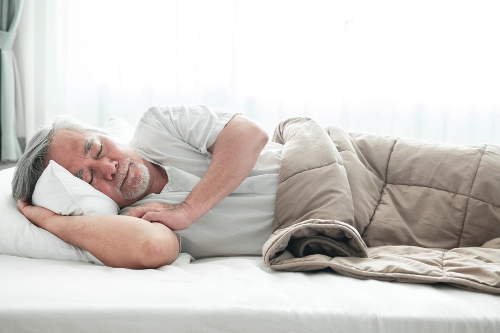 A senior man lying down with a weighted blanket