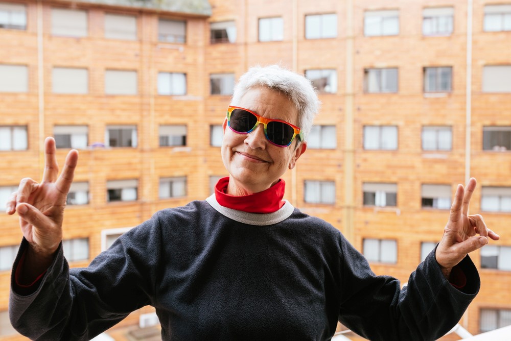 A gay granny wearing sunglasses by an apartment building