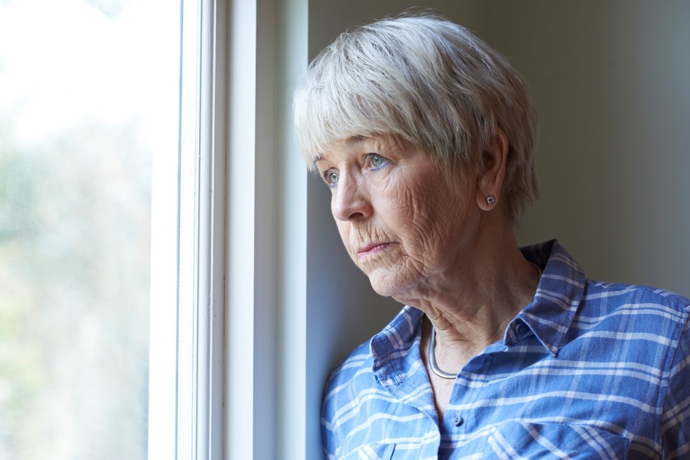 A negative elderly woman with depression looking out the window. She may also be diabetic and struggling to manage her condition. 