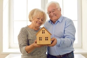 Two elderly parents holding a model of a house, highlighting the idea of talking to aging parents about moving