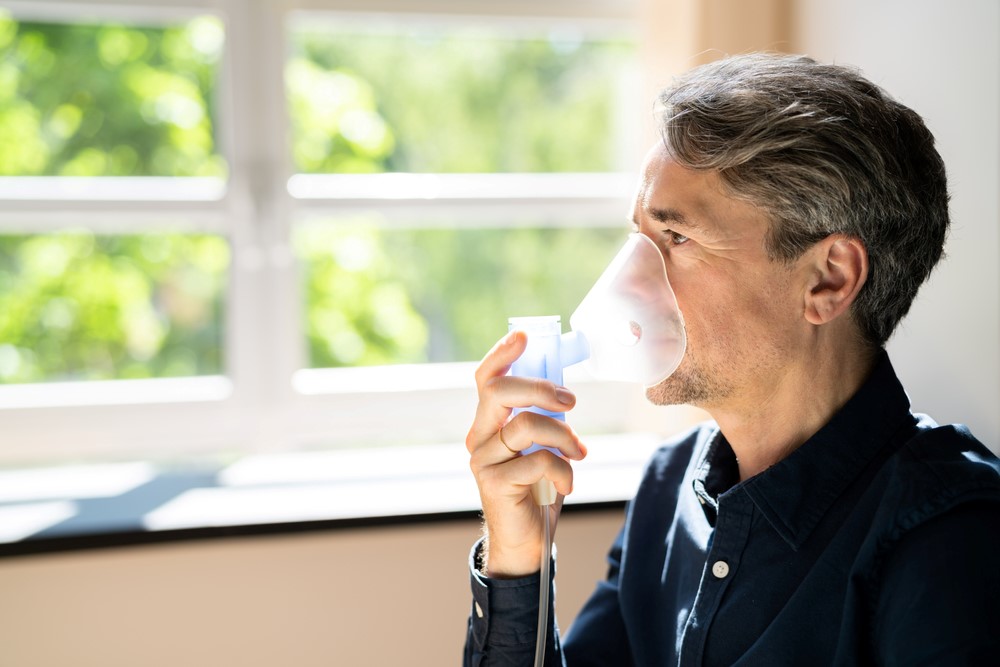 A senior man holding a nebulizer to his face