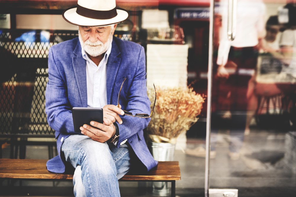 A well dressed senior man using a tablet outside