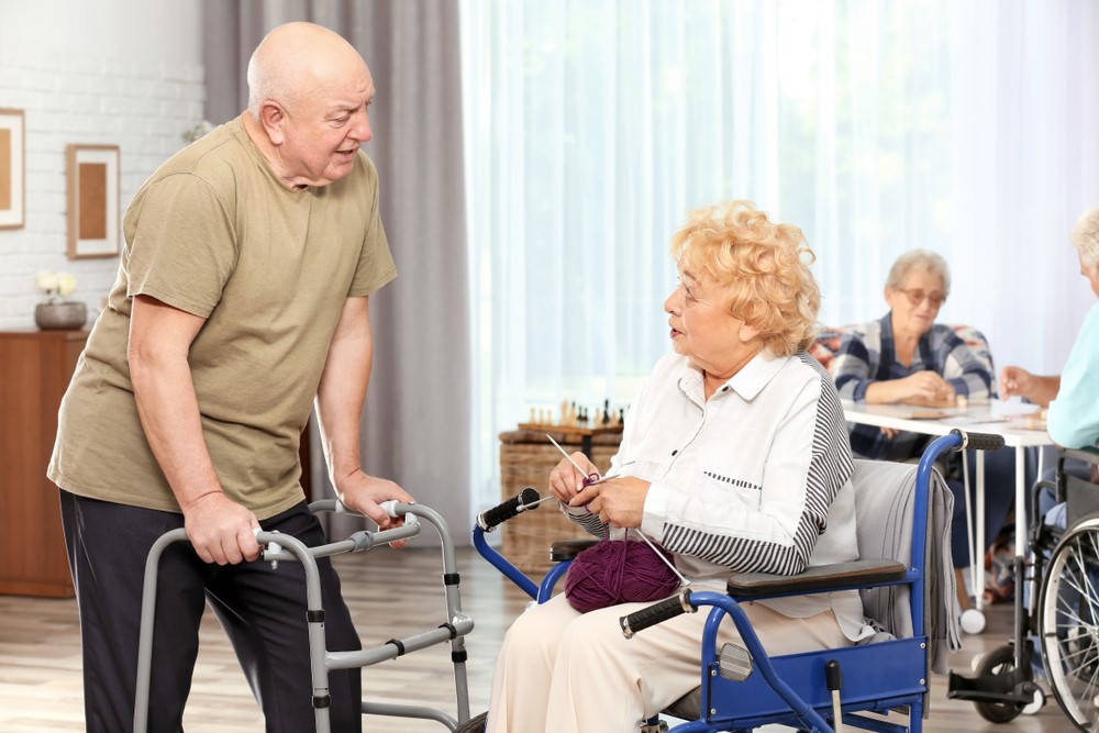 Various seniors in a nursing home, including an elderly man using a walker and a woman in a wheelchair