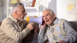 A man using a bullhorn to talk to another, illustrating the idea of hearing aids vs hearing amplifiers