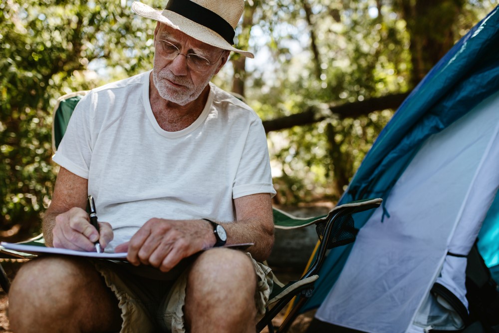 A senior man writing in a journal at a campsite