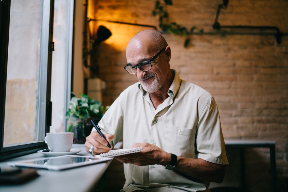 A senior poet writing in a journal in a cafe