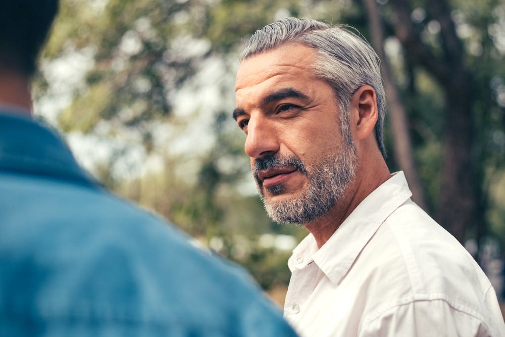 An elderly man sitting outdoors, talking to his son about assisted living or other housing options