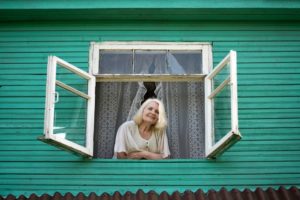 A senior woman looking out of a window after being isolated