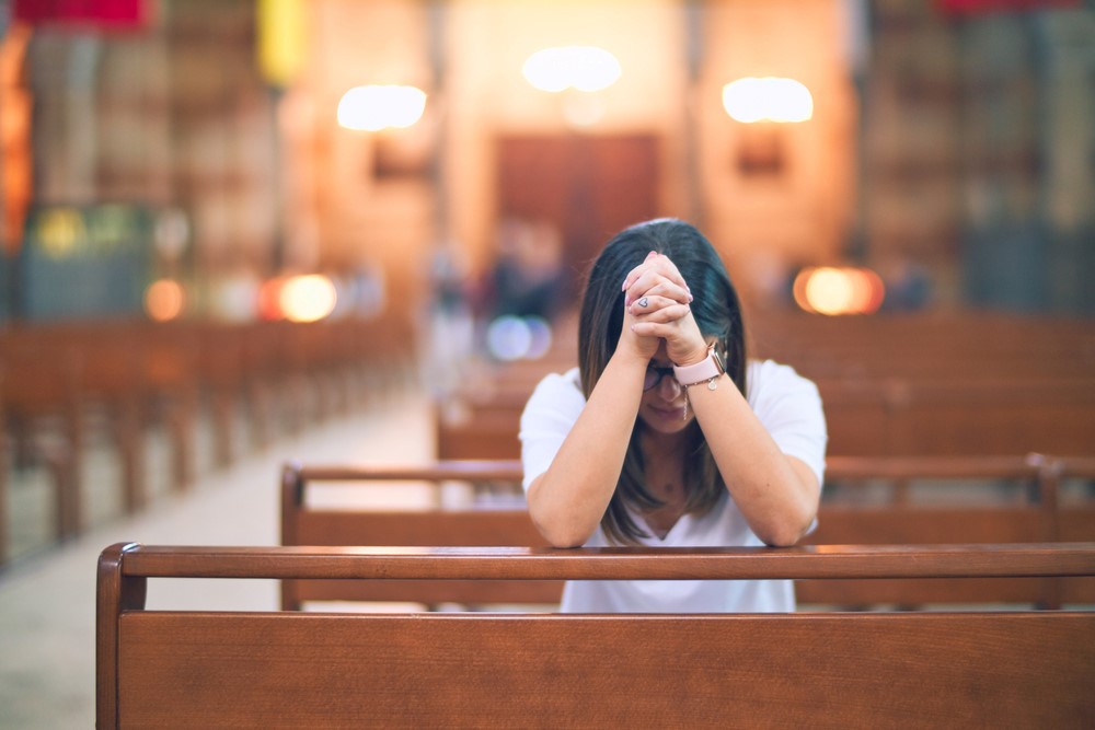 A Hispanic woman praying in a church, highlighting the idea of bible verses for caregivers