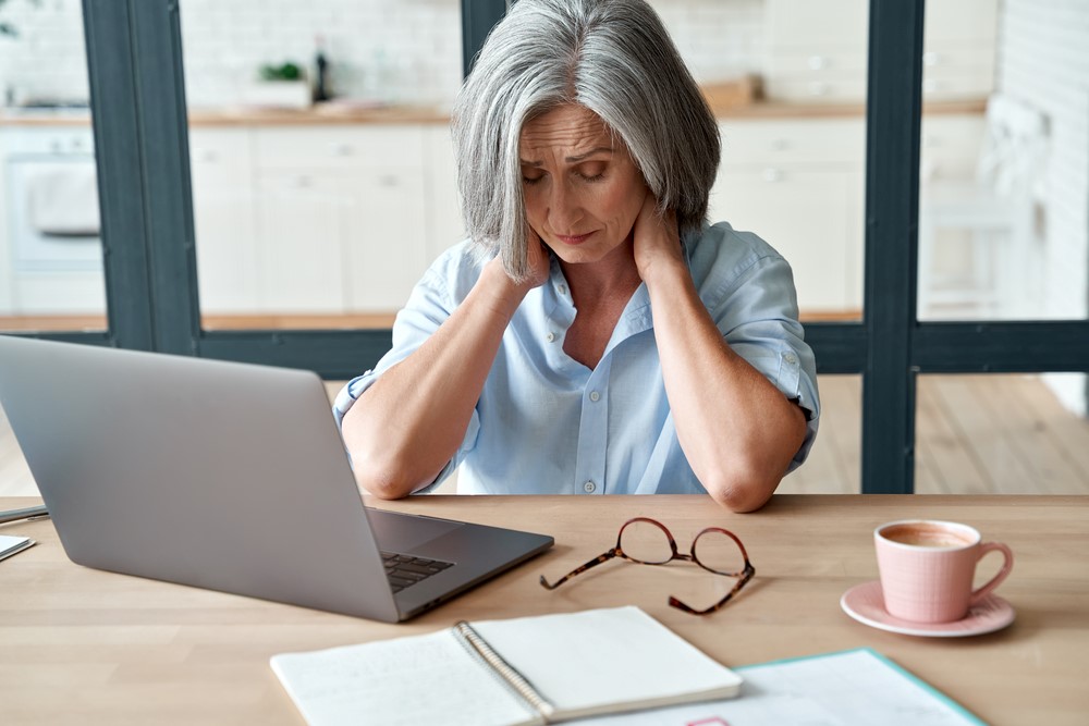 A senior woman holding her neck, looking at online therapy