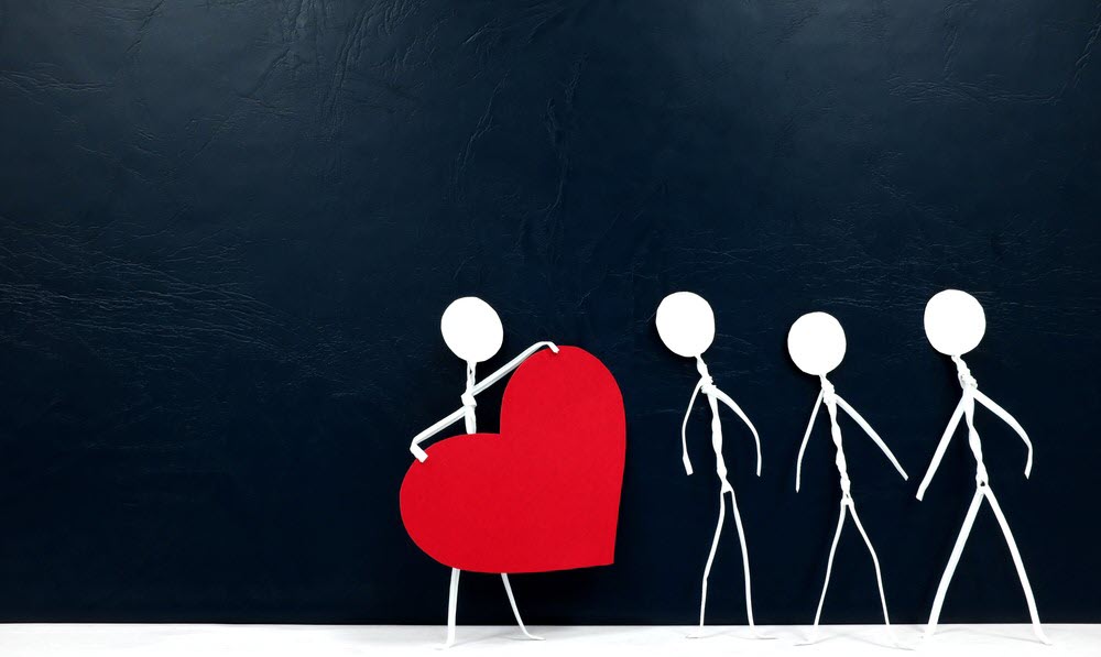 A stick figure holding a heart, next to three others, highlighting the idea of compassion