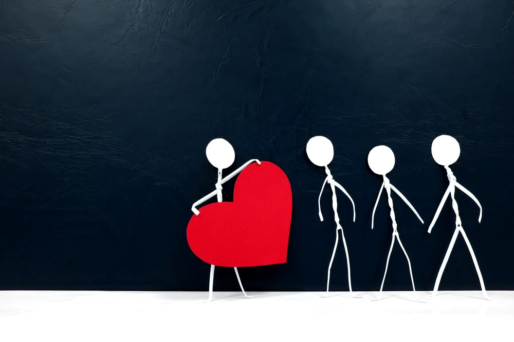 A stick figure holding a heart, next to three others, highlighting the idea of compassion