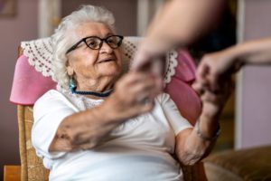 A senior being helped from her chair by a caregiver