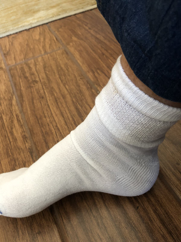 Someone wearing a white Dr. Scholl's sock on a wooden floor