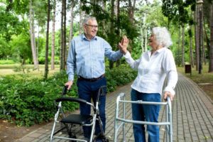 A senior couple using mobility aids outside and giving each other a high five