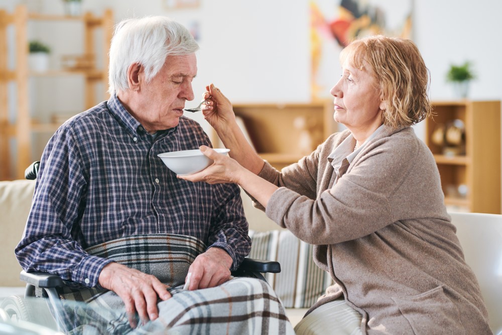 An elderly woman helping her husband to eat, highlighting the idea of spouse caregiver loneliness