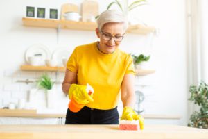 An older woman in a yellow shirt cleaning at home, highlighting the idea of the best kitchen cleaners for asthma
