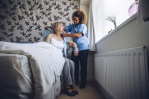 A caregiver helping a woman out of bed, highlighting the benefits of a life-in caregiver