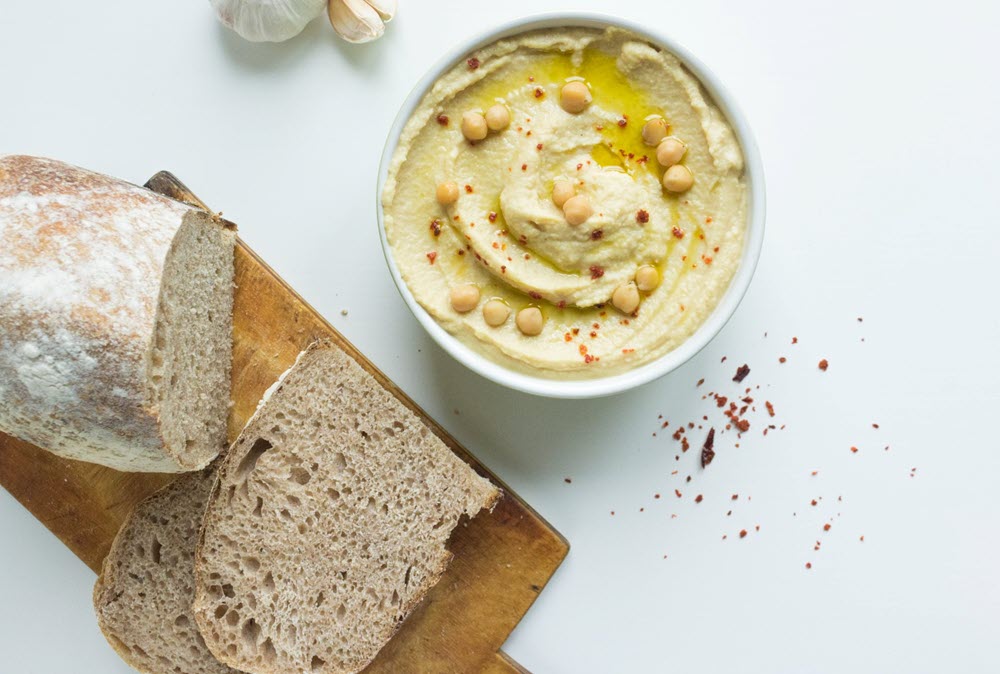 A loaf of fresh soft bread next to a bowl of hummus