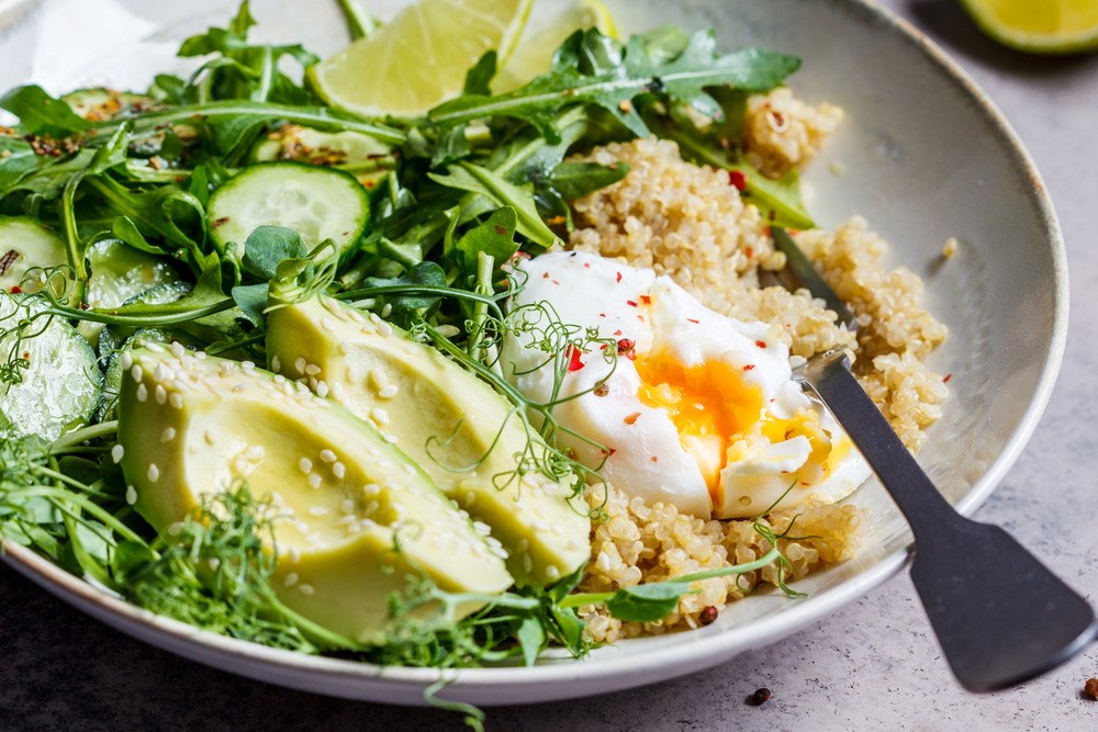 A white bowl containing couscous, egg, avocados and greens