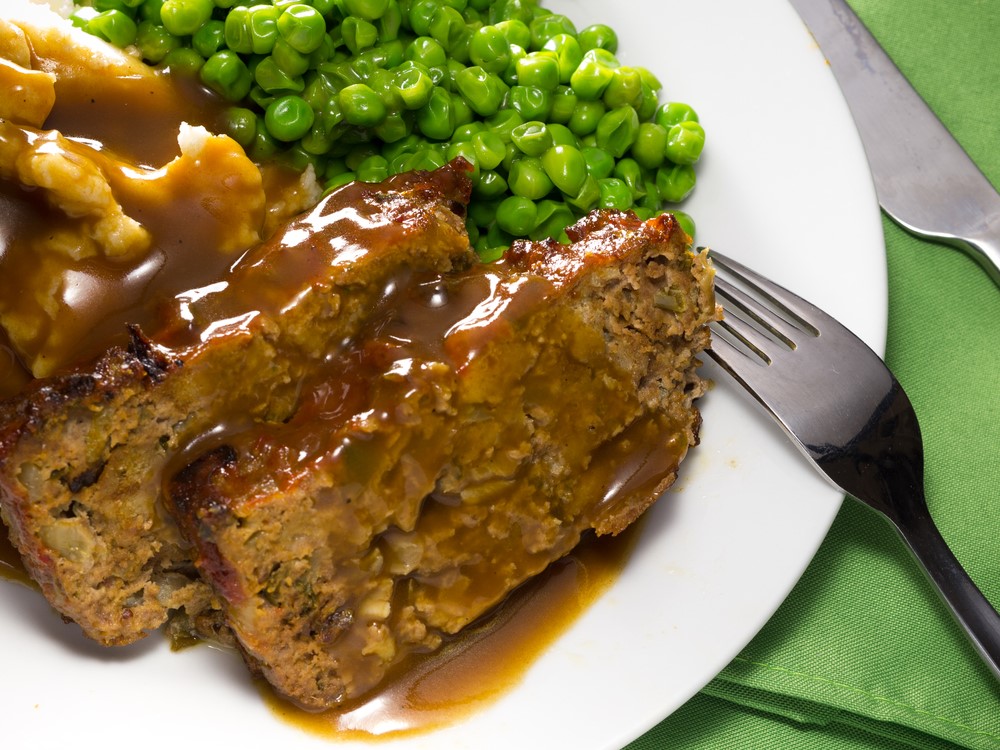 A white plate with meatloaf, gravy, mashed potatoes, and peas, as an ideal soft food for elderly with no teeth