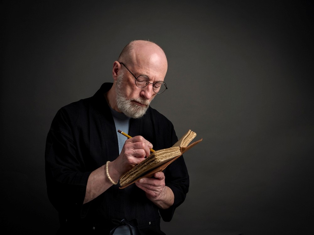 An older bald man writing in his journal