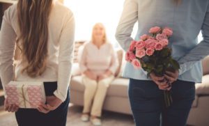 Two adult children or teenagers holding gifts for someone in assisted living behind their backs