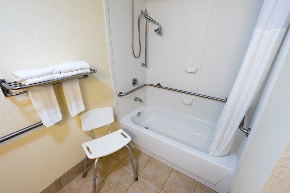 A bathroom with a stool and grab bars on the wall